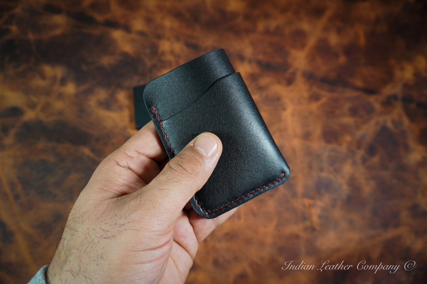 Back view of Handcrafted Outrider EDC wallet made from black Italian Veg Tanned leather, shown in hand with wrap-around minimalist design