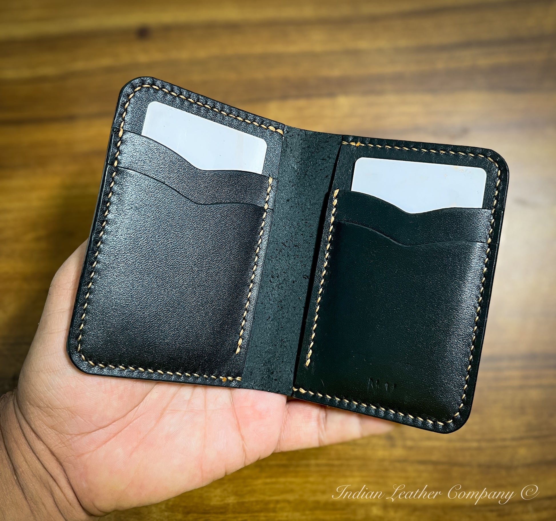 A top-down view of the wallet's interior, featuring two vertical pockets and two hidden compartments. The leather is displayed in a warm, natural tone, with visible stitching along the edges.