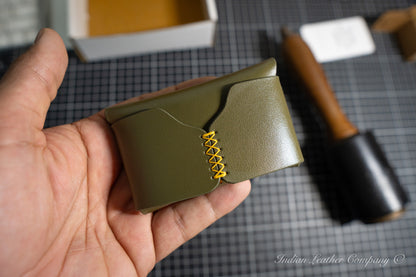 Hand holding a green full grain veg tanned leather wallet with yellow stitching on a checkered surface.