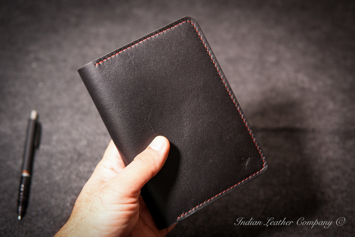 A hand holding a black leather journal cover with red contrast stitching made by indian leather company
