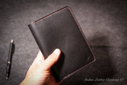 A hand holding a black leather journal cover with red contrast stitching made by indian leather company