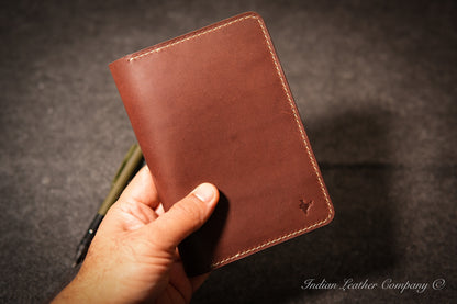 A hand holding a brown leather Journal holder with visible saddle stitching and a small embossed logo